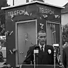 John Giæver, lederen av Telefonsøkendes Landsforening, avduket en blomsterprydet telefonkiosk med TV-vist tale og orkestermusikk. Foto: NTB