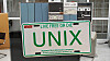 Bilskilt brukt i markedsføringen av UNIX, foran et tilsvarende system som det Unix først ble utviklet for – DEC PDP-7 – fotografert ved Universitetet i Oslo i 2005.