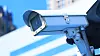 Camera system guarding blue skyscraper office building with sky above
