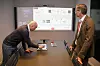 Ved et enkelt trykk på styringsenheten fra Cyviz på egen arbeidsstasjon kan datastrømmen/datakildene vises på skjermen i møterommet ved hjelp av tilsvarende styringsenhet der. – Du trenger ikke ta med egen pc til møterommet, sier Harald Bøe fra Cyviz (t.h.) mens Bjørn Olav Bådsvik henter fram aktuelle kilder. Foto: Alf Bergin